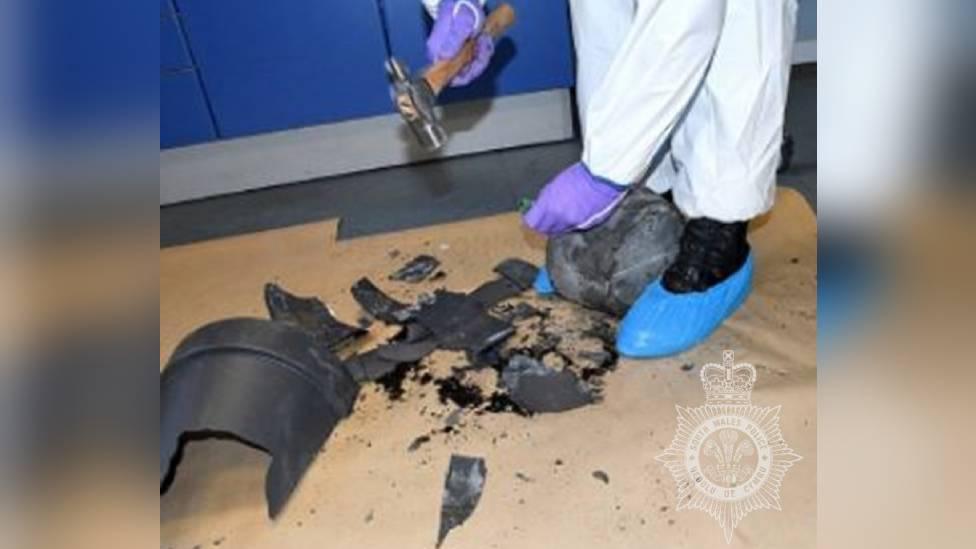 A forensics officer smashing open the plant pot containing the gun