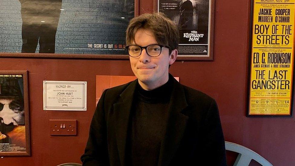 A man dressed in black clothes stands in front of old movie posters