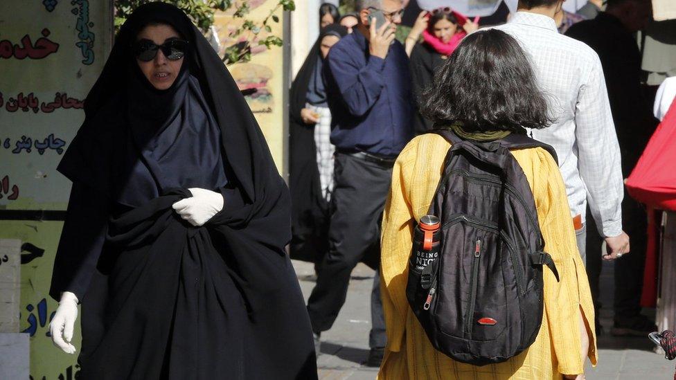 A girl with her hair uncovered walks past a veiled woman on a street in Tehran, Iran (13 September 2023)