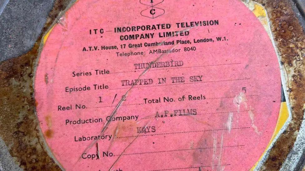 A rusty metal container with a pink label on it saying the material inside is from an episode of Thunderbirds called Trapped In The Sky. It has branding on it from 'Incorporated Television Company Limited'.