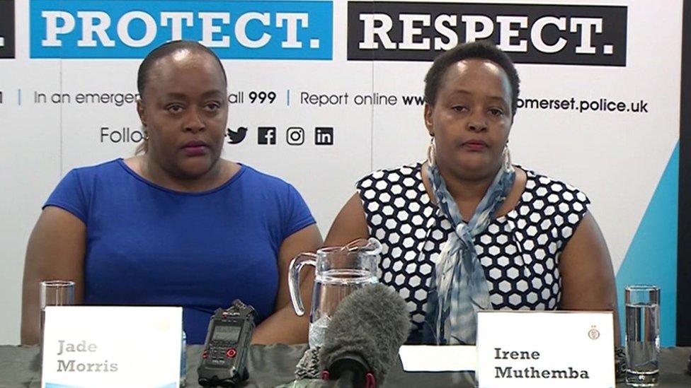 Two black women sitting next to each other, one in a blue top and one in spotty white and black top