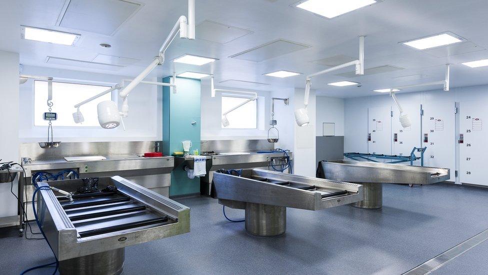 Inside of mortuary showing three mortuary tables with lights above them