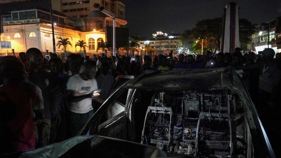 People stand around a car that was burned by supporters of the Unity Party and Liberia's newly-elected President Joseph Boakai, after it plowed into them while they were celebrating Boakai's win, in Monrovia, Liberia November 20, 2023