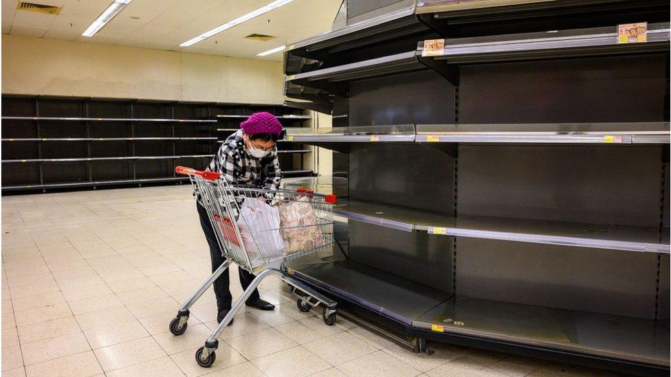 A shopper stands next to empty supermarket shelves in Hong Kong