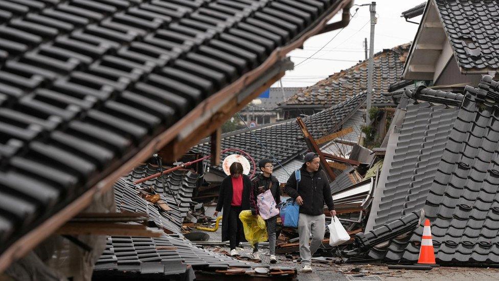 Three people walking through a town in Japan devastated by a tsunami