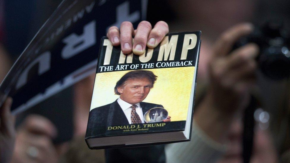 Man holds up a book by Donald J. Trump at a campaign rally.