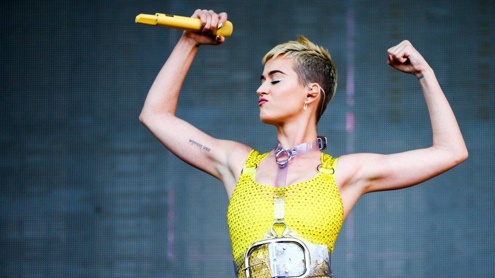 This is a photo of singer Katy Perry performing and flexing her muscles.