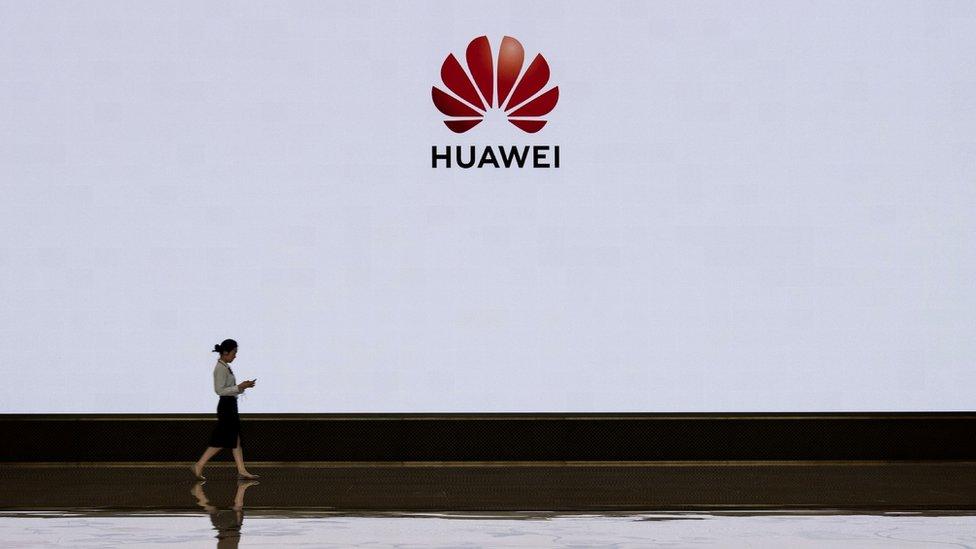 A member of Huawei's reception staff walks in front of a large screen displaying the logo in the foyer of a building used for high profile customer visits and displays at the company's Bantian campus on April 12, 2019 in Shenzhen, China.