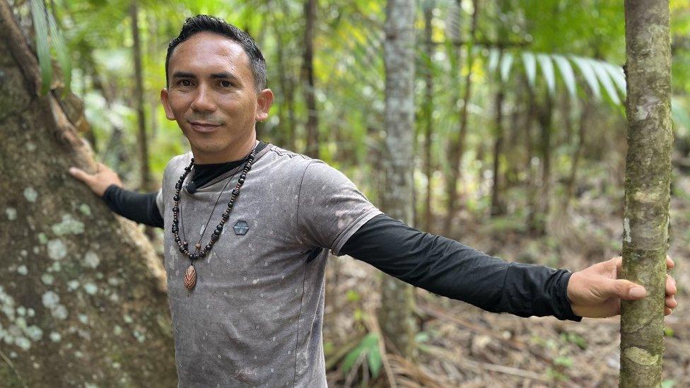 Robson Gonçalves Machado, who lives on the banks of the River Acangatá in Brazil. He is a young man and is wearing a grey t-shirt and a beaded necklace.