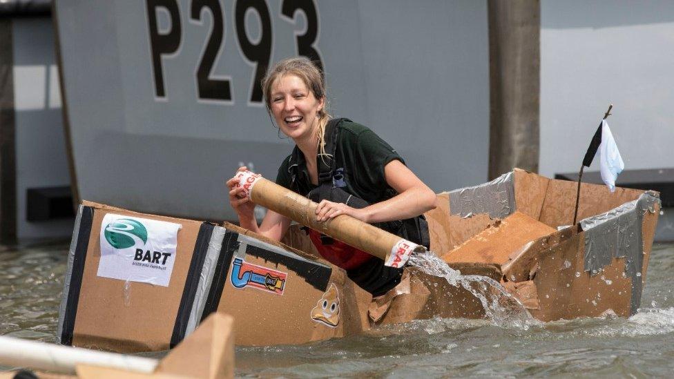 A woman racing in last year's competition - she is directing a carboard boat in the harbour