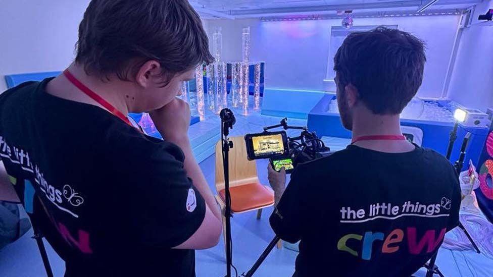 Two crew members set up a camera shot in a blue lit sensory room at the hospice