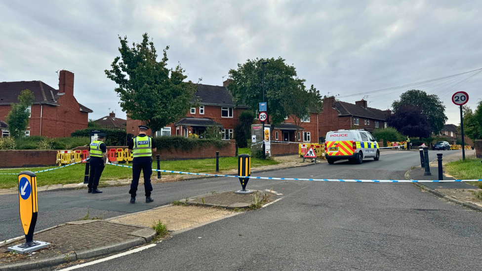 Two police officers stand in front of a cordon at the top of Bellfarm Avenue