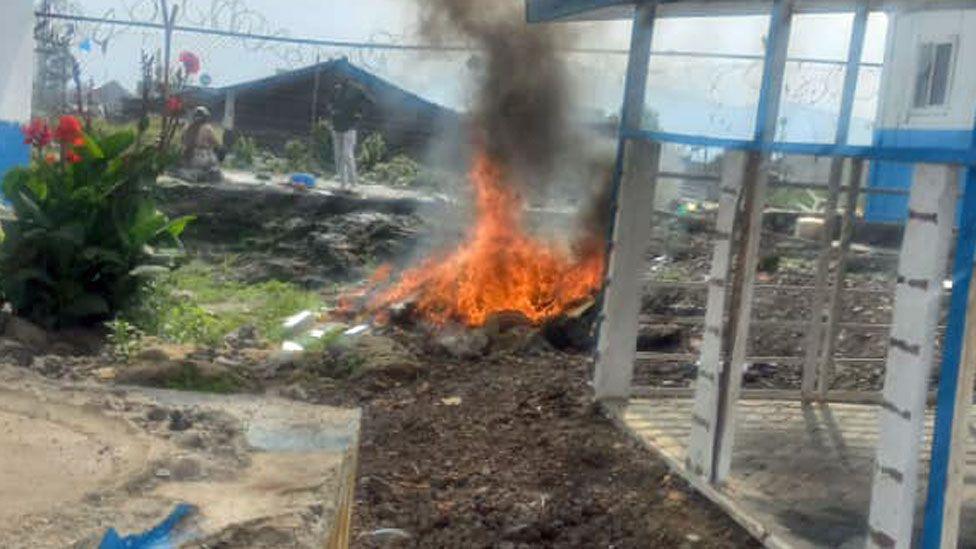 A man in the background can be seen with hands on hips gazing at a fire burning outside Bisengimana hospital in Goma after it was looted last month