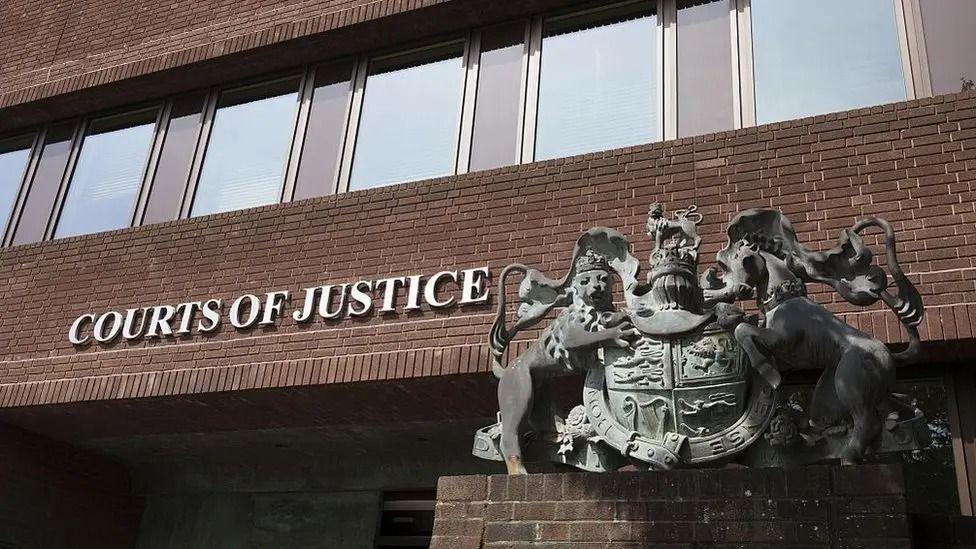 The exterior of Portsmouth Crown Court - a brown brick building with the words 'Courts of Justice' and a metal sculpture of the royal crest