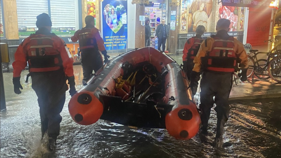 Firefighters carry a rescue dinghy through flood water in Blackheath