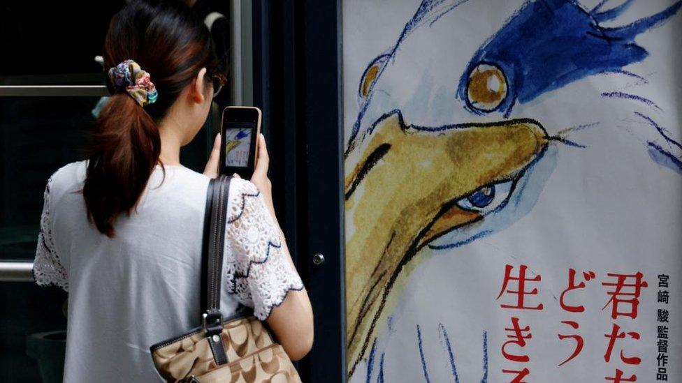 Woman photographing a poster of the Boy and the Heron