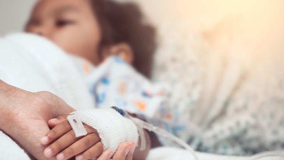 Mother holding a child patients hand in a hospital bed