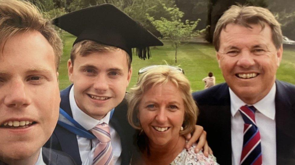 Jack wearing his graduation robe and cap, standing alongside his mum, dad and older brother, Ben