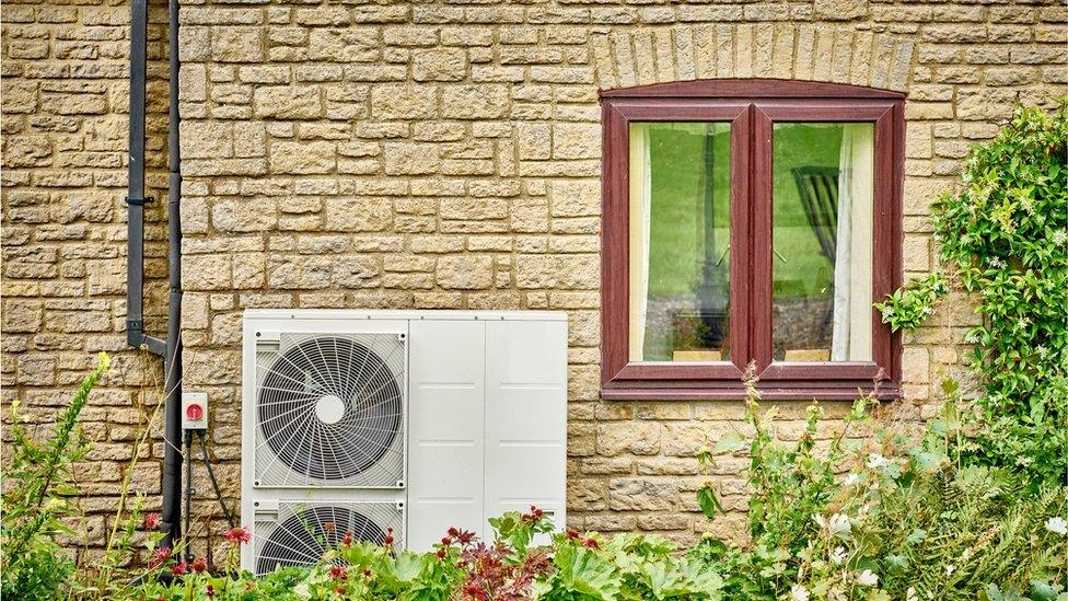 Air source heat pump on the outside of a brick building with a window to the right