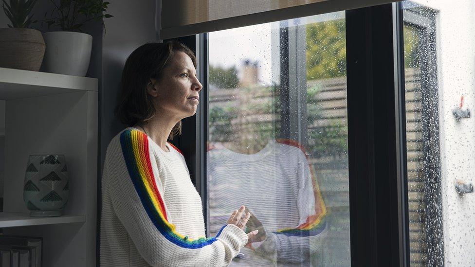 A woman looks hopelessly out of a rainy window