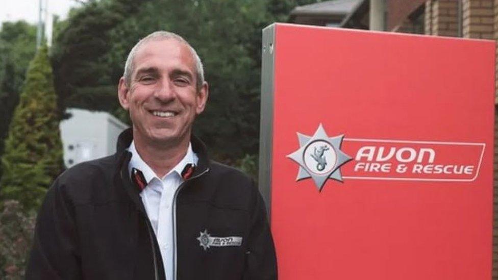 A man smiling at the camera in front of a fire service sign