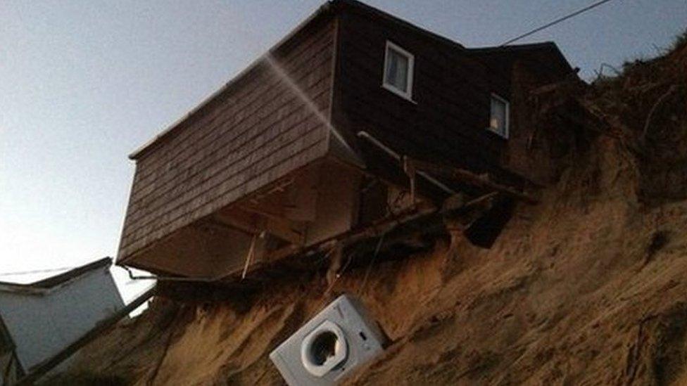 A beach chalet hanging over a beach after the ground beneath it collapsed