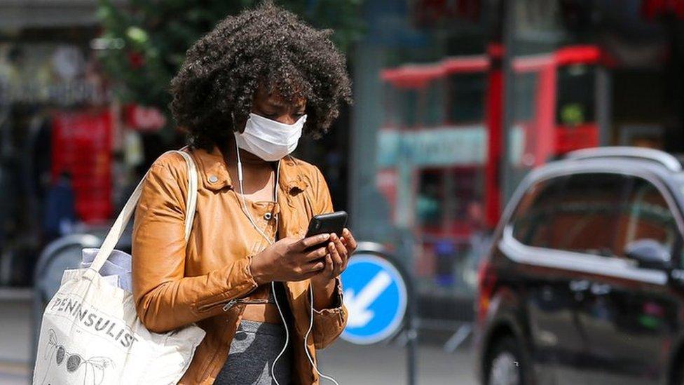 A woman wearing a face mask is seen using a mobile phone while walking on the street.