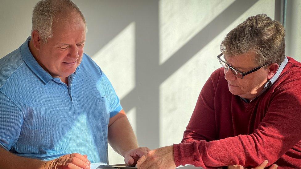 Malcolm Sibthorpe sitting at a desk with Alistair rush, looking through some paperwork.