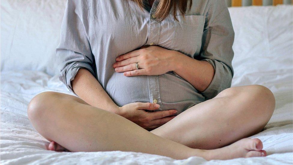 Pregnant woman sitting on bed at home holding her bump