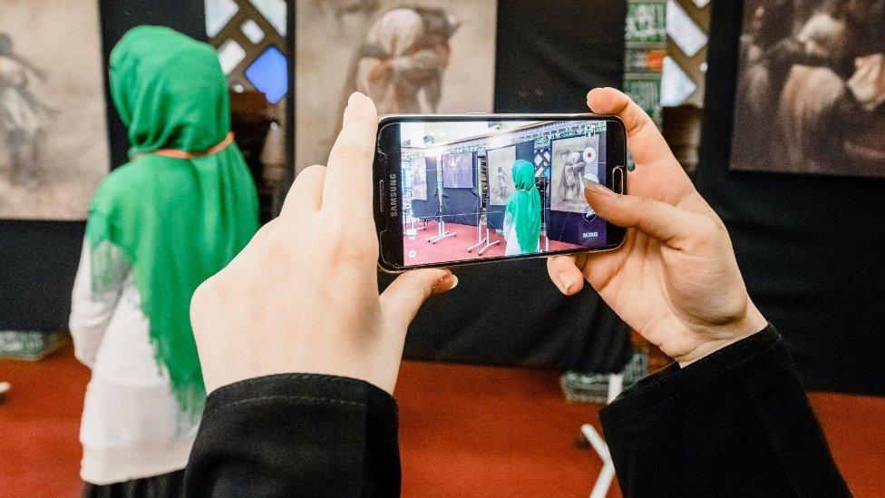 A woman takes pictures of another woman wearing a headscarf and looking at a picture cycle on display at the Blue Mosque in Hamburg, northern Germany, on October 3, 2016, which marks the Open-Mosque-Day.