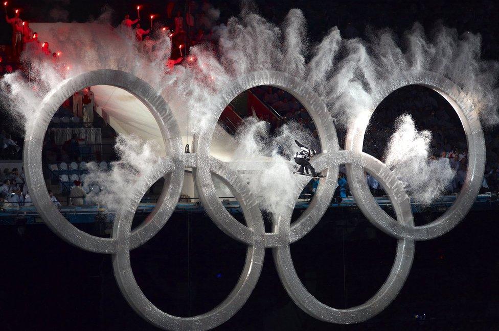 Johnny Lyall leaps through Olympic Rings as snow comes from them.