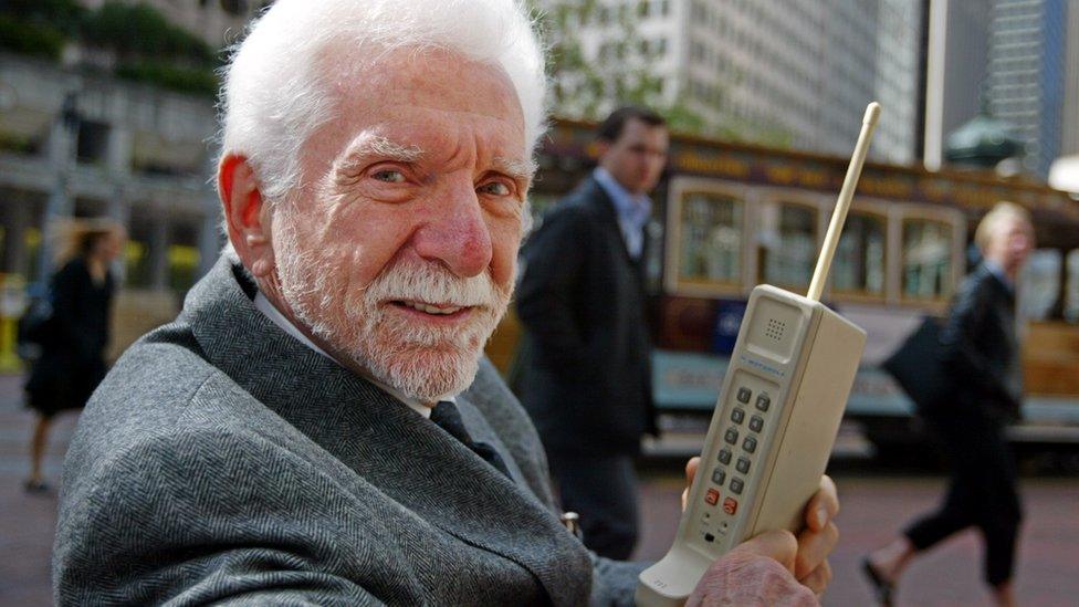 Martin Cooper holding a mobile phone from 40 years ago