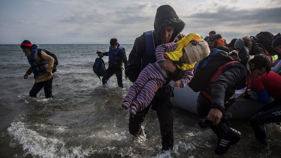 Refugees and migrants disembark a dinghy after arriving on the island of Lesbos from Turkey