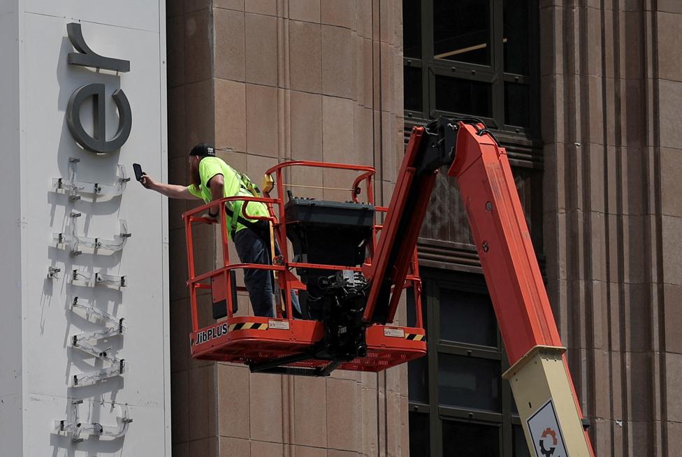 A worker uses a smartphone while dismantling a Twitter's sign at Twitter's corporate headquarters building as Elon Musk renamed Twitter as X and unveiled a new logo, in downtown San Francisco, California, U.S., July 24, 2023.