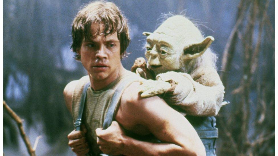 Still from Star Wars, the character Yoda, sits on Luke Skywalker's back.