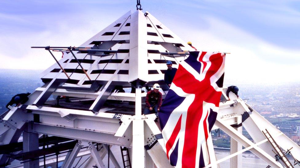 A steel worker pulls at the Union Jack suspended from the pyramid top of One Canada Square.