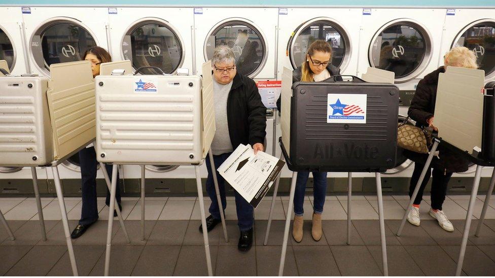 Several people are shown standing in voting booths in a Laundromat