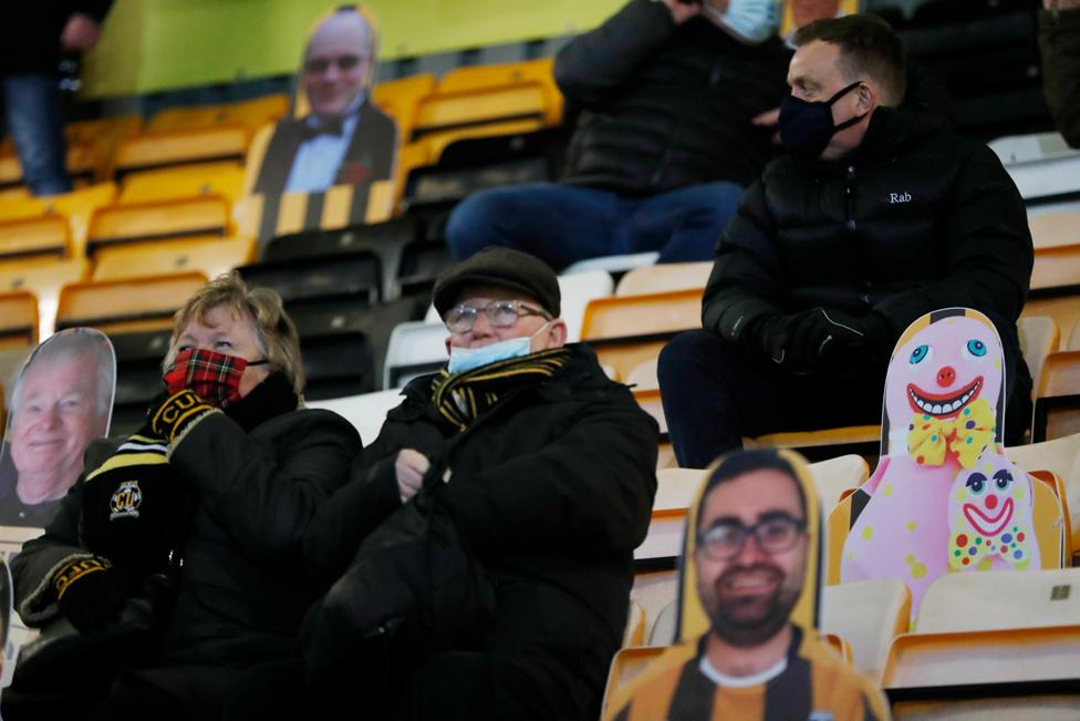 Football fans sit in the stands next to cardboard cut-outs