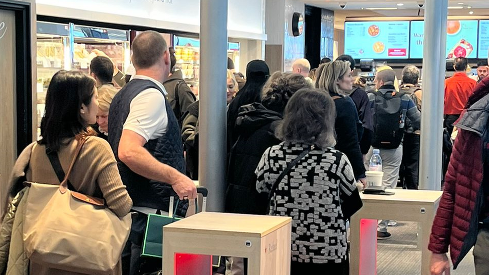 A long queue of people at a sandwich shop