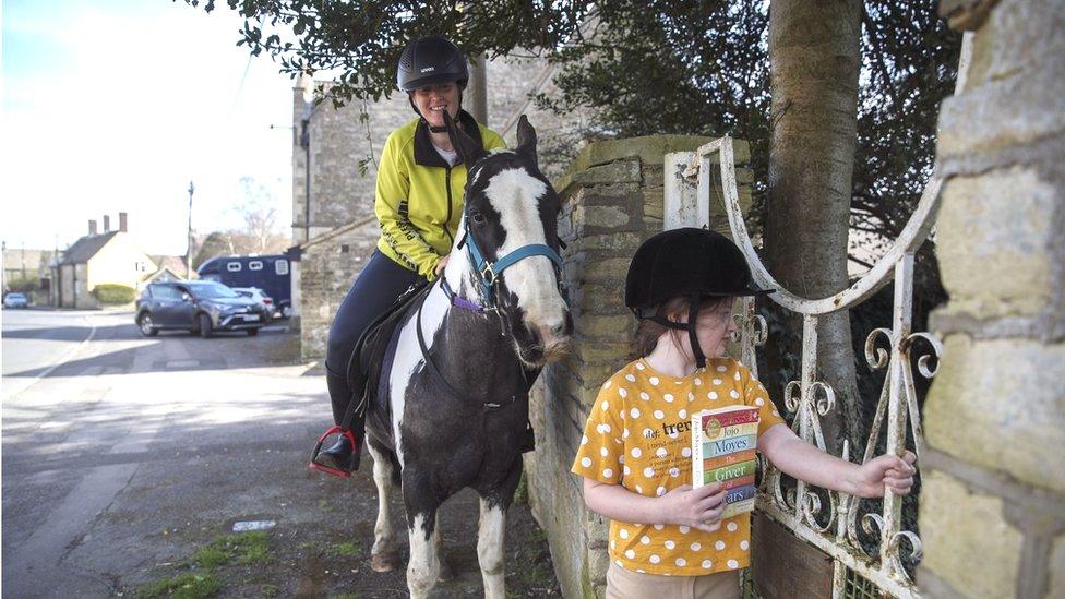 Rescue pony Micky helps owner Abi Eliot-Williams and her daughter Polly, deliver library books to members of the Hullavington Book Group in the village of Hullavington near Malmesbury, Wiltshire.