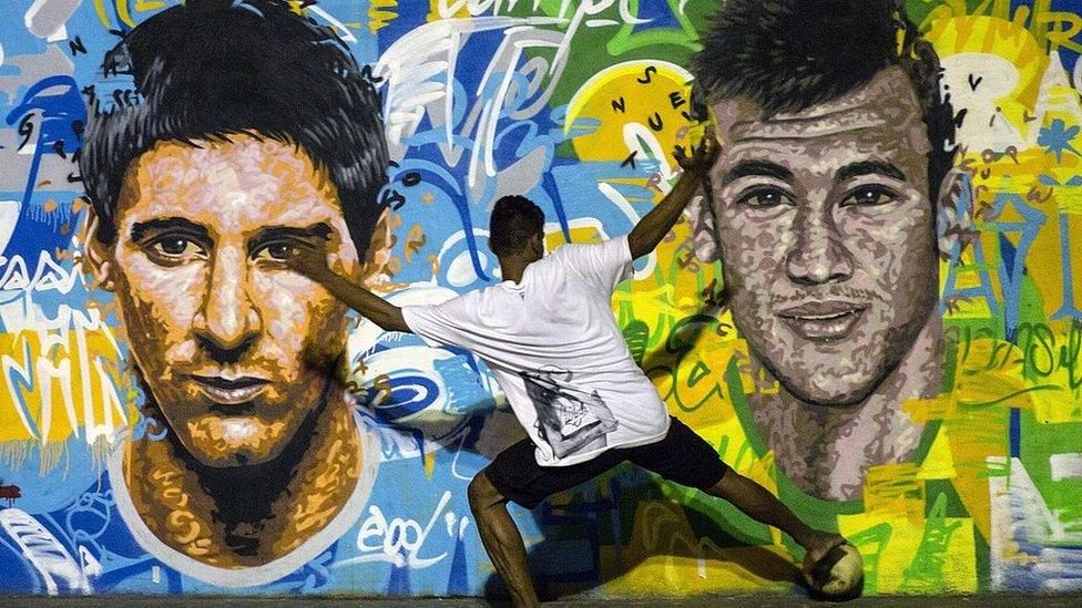 Youngsters play football in front of a mural of Argentine football player Lionel Messi (L) and Brazil's player Neymar da Silva Santos Junior at a field of Tavares Bastos shantytown (favela) in Rio de Janeiro, Brazil