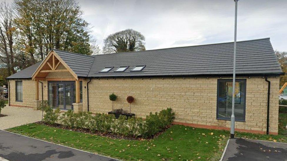 The community shop and café in Cotswold-style stone, a one-storey building with wooden porchway, newly built.