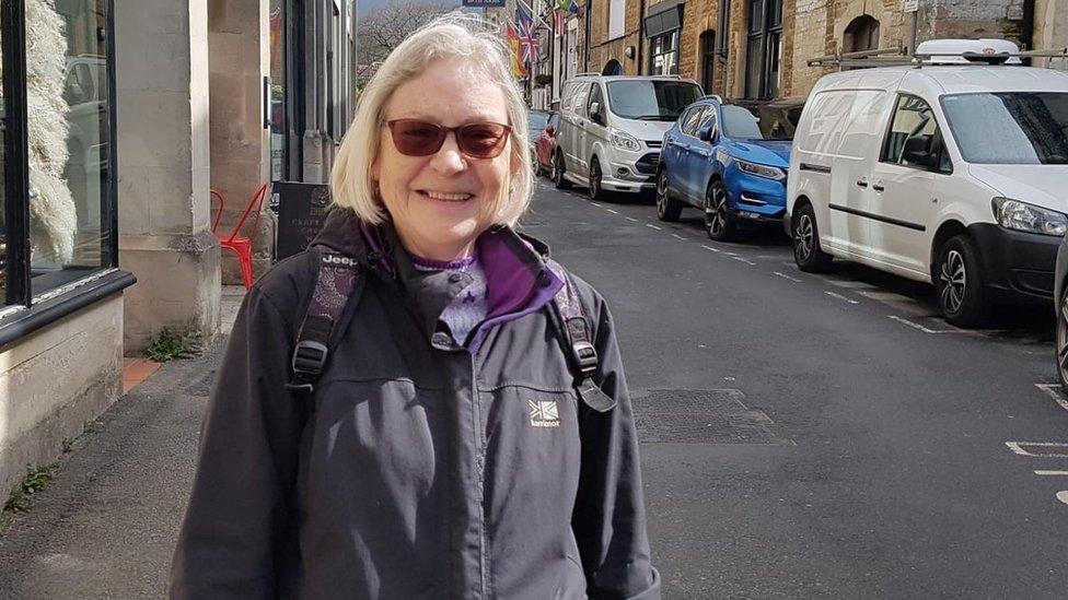 Jackie wearing tinted glasses and smiling by a road with cars parked on it