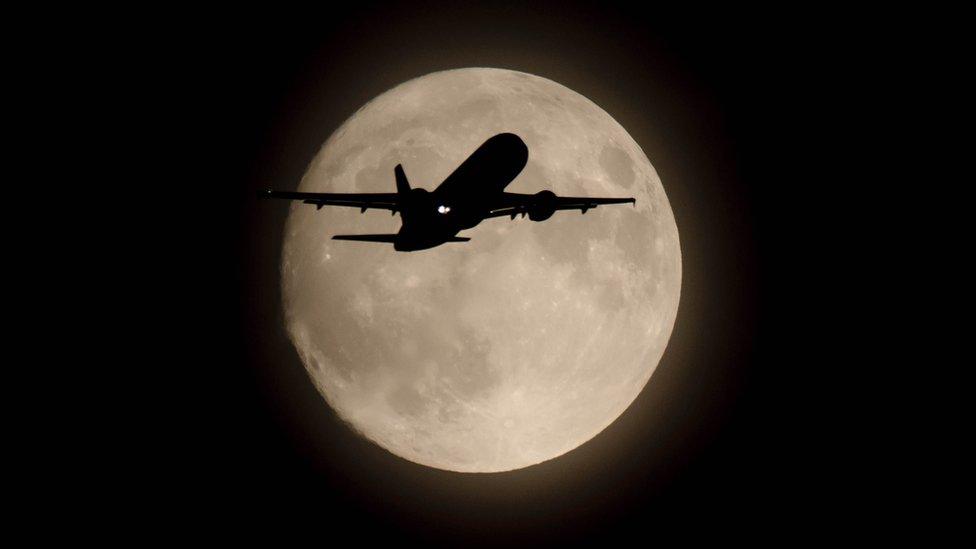 A plane flies in front of the full moon