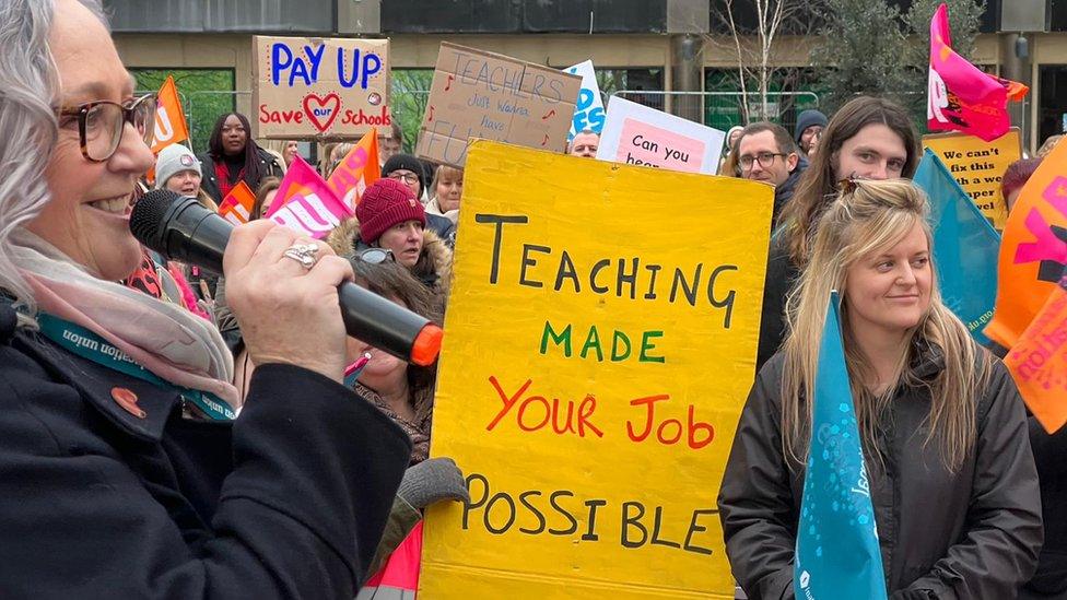 Debbie Brown holding a sign that says 'teaching made your job possible'