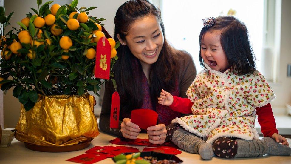 Woman decorating tangerine tree with red envelopes