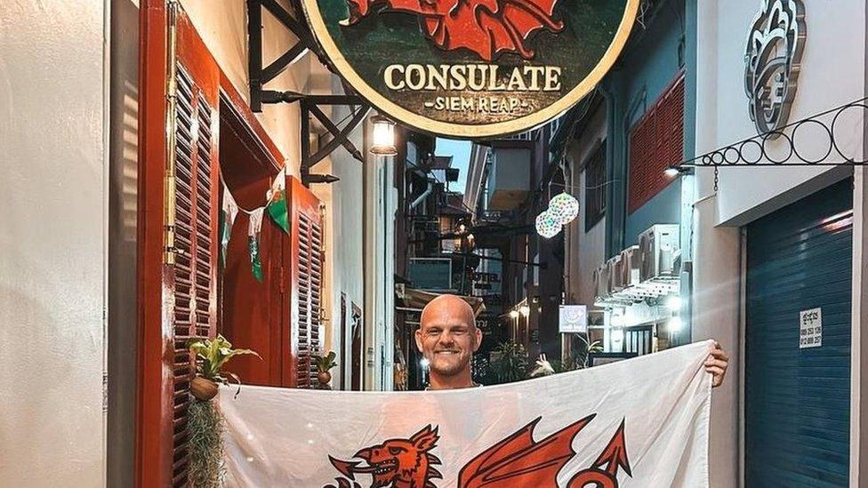 Luke Jones holds a Wales national flag inside the Welsh Consulate pub in Siem Reap