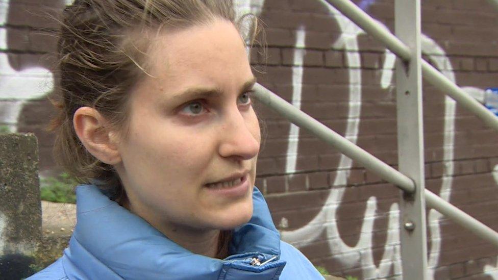 Image of Jen with her hair pinned back, wearing a light blue puffer jacket in front of some concrete steps.