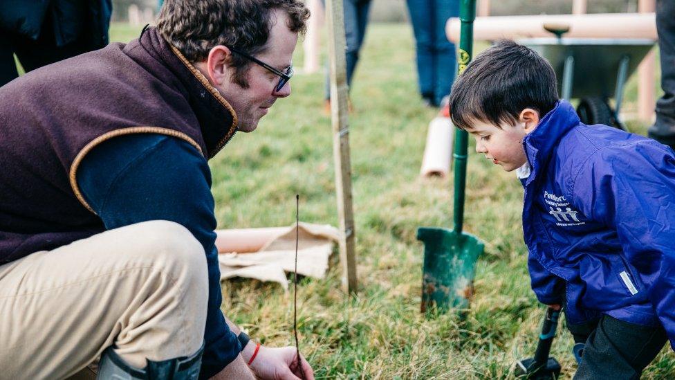 A man and an young boy kneeling on the grass to plant seeds