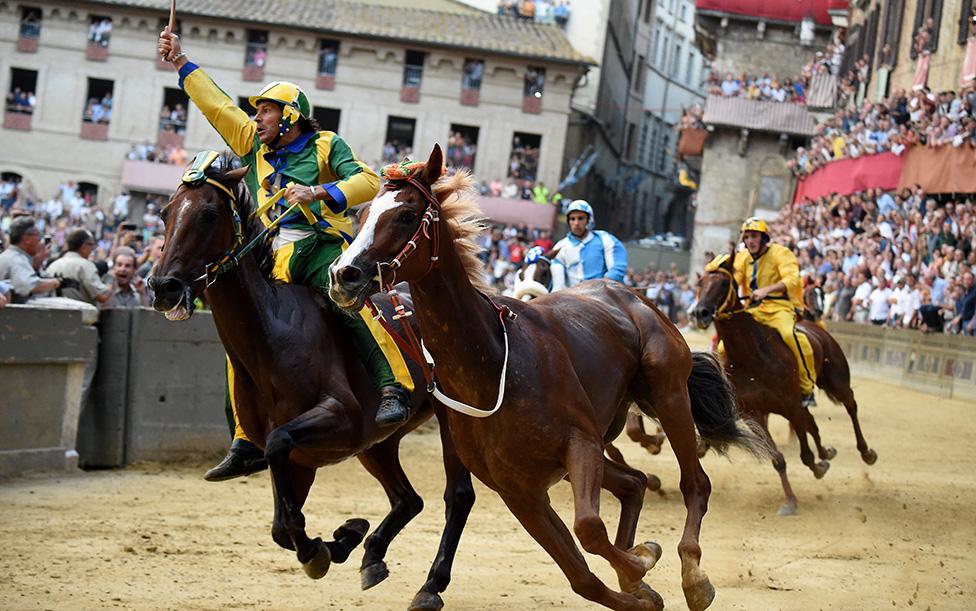 Riderless horse Remorex of Selva Contrada team (C) passes Bruco Contrada team horse Schietta ridden by Andrea Mari known as Brio to win during the historical Italian horse race "Palio di Siena" on August 16, 2019 in Siena